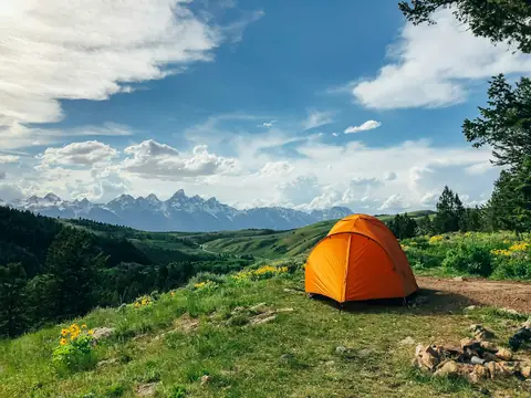 Orange tent pitched on a grassy hillside below mountains